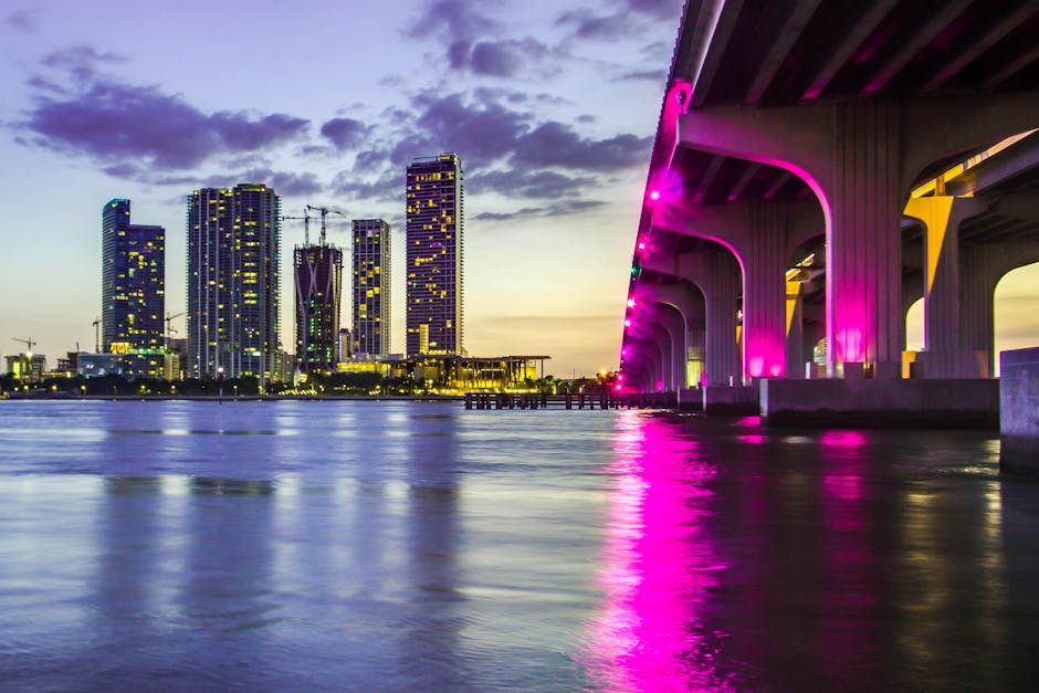 Captivating view of Miami skyline and illuminated bridge reflecting on water at dusk, vibrant city lights aglow.